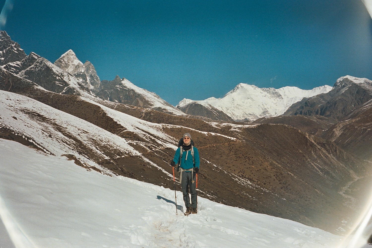John trekking with walking poles beneath snow-covered Himalayan peaks in Nepal